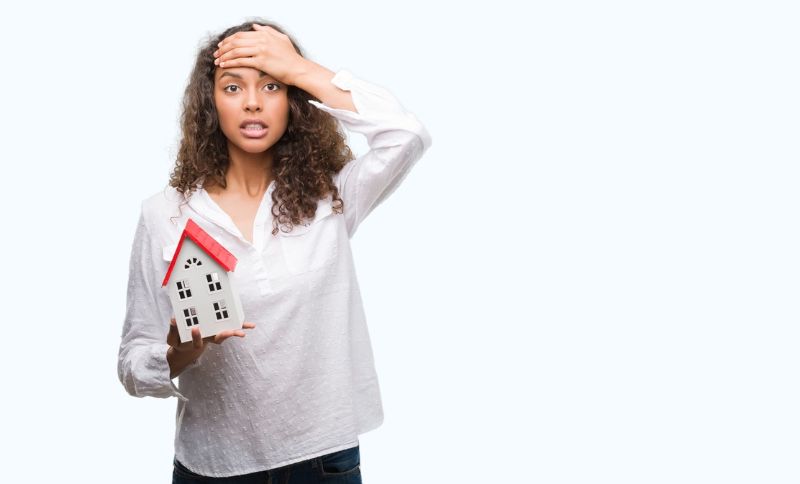 a woman holding a mini house model and her forehead