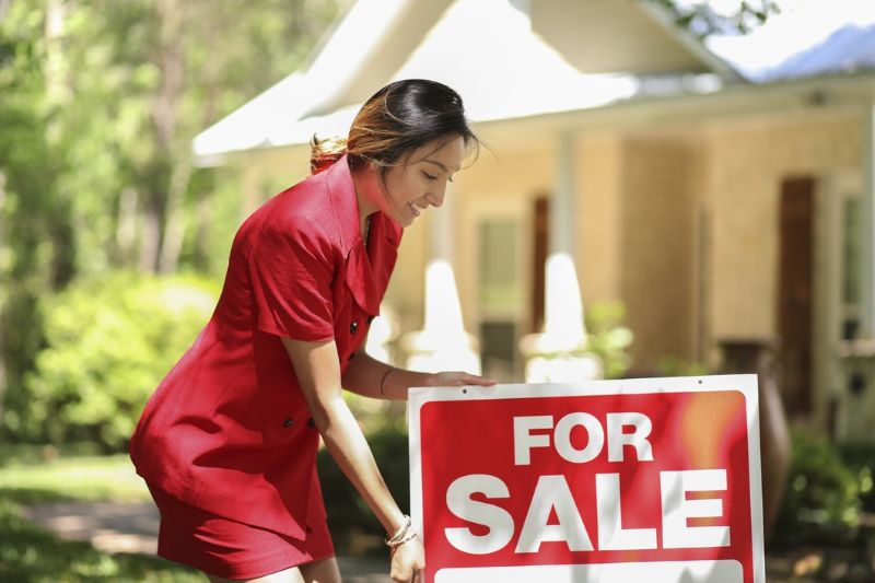 a woman in red dress beside the 'for sale' signage