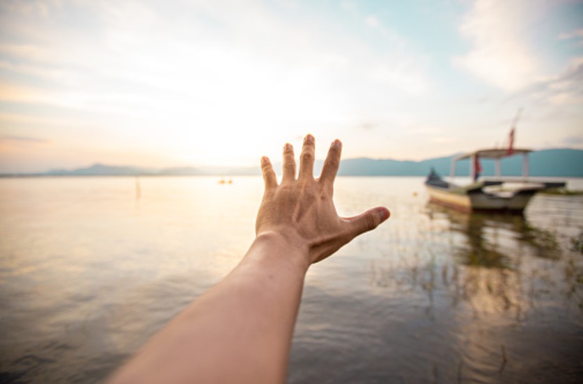 Hand reaching for the horizon during sunset