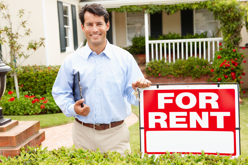 Landlord standing beside a For Rent sign
