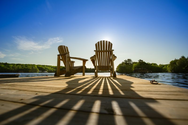 Two empty adirondack chairs sitting on a dock while sunrise